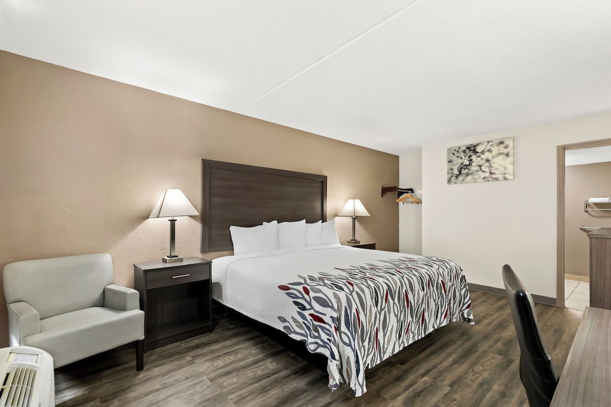 A hotel room with a bed, two bedside tables with lamps, a chair, a desk, and a small table.