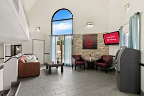 A modern hotel lobby with a large arched window, a Red Roof Inn sign, a flat-screen TV, and a self-service kiosk. - Red Roof Inn & Suites Duncan (Duncan)