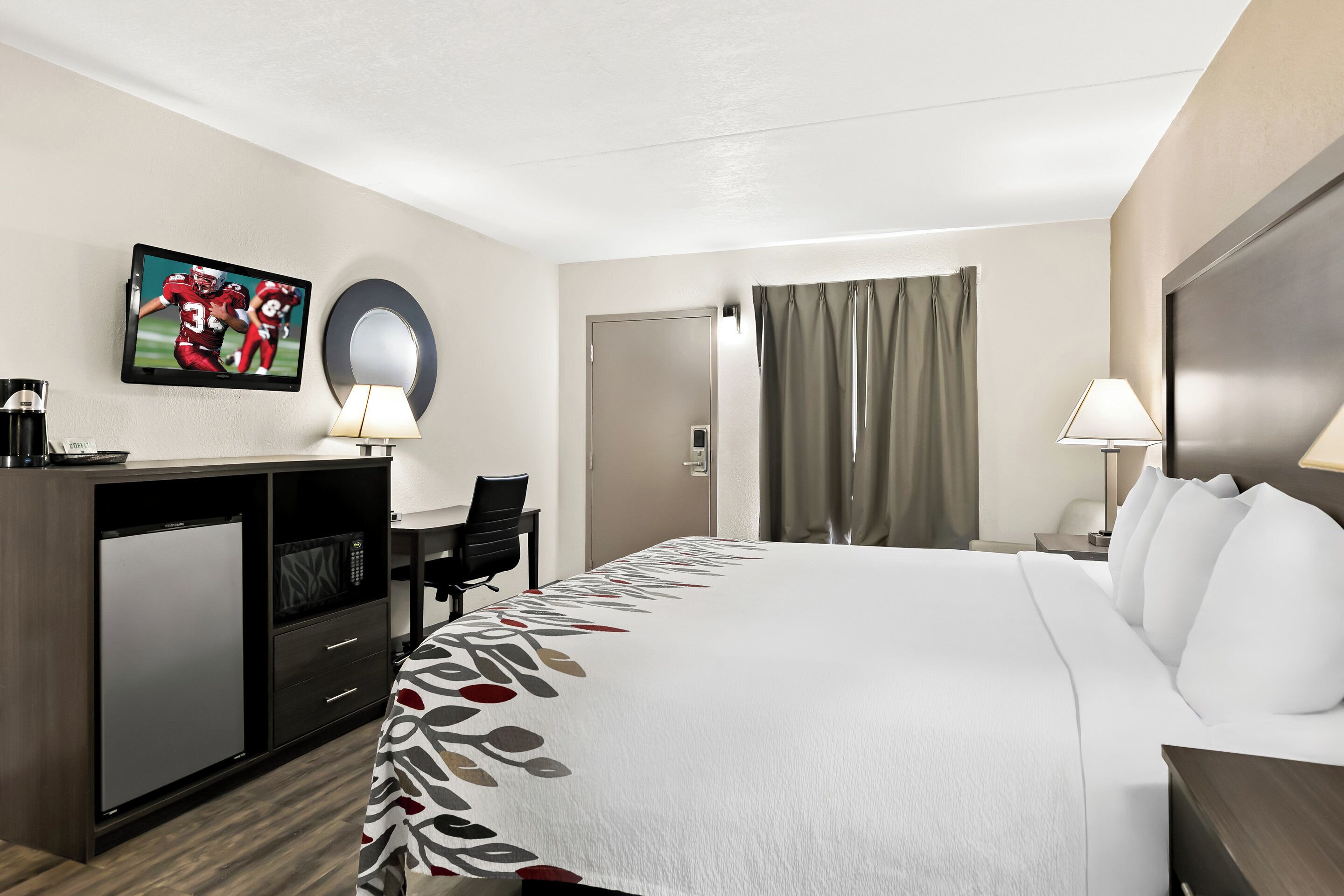 A hotel room with a bed, desk, and television.