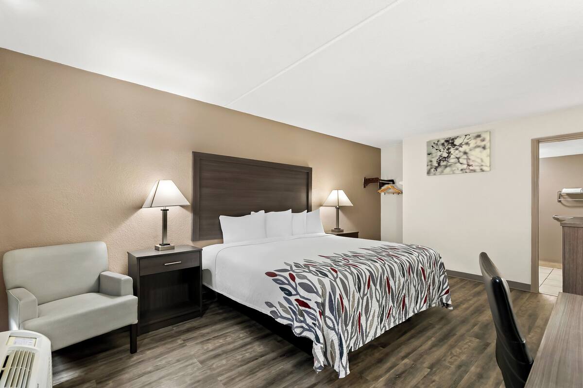 Ein Hotelzimmer mit einem Bett, zwei Nachttischen mit Lampen, einem Sessel, einem Schreibtisch und einem kleinen Tisch.
