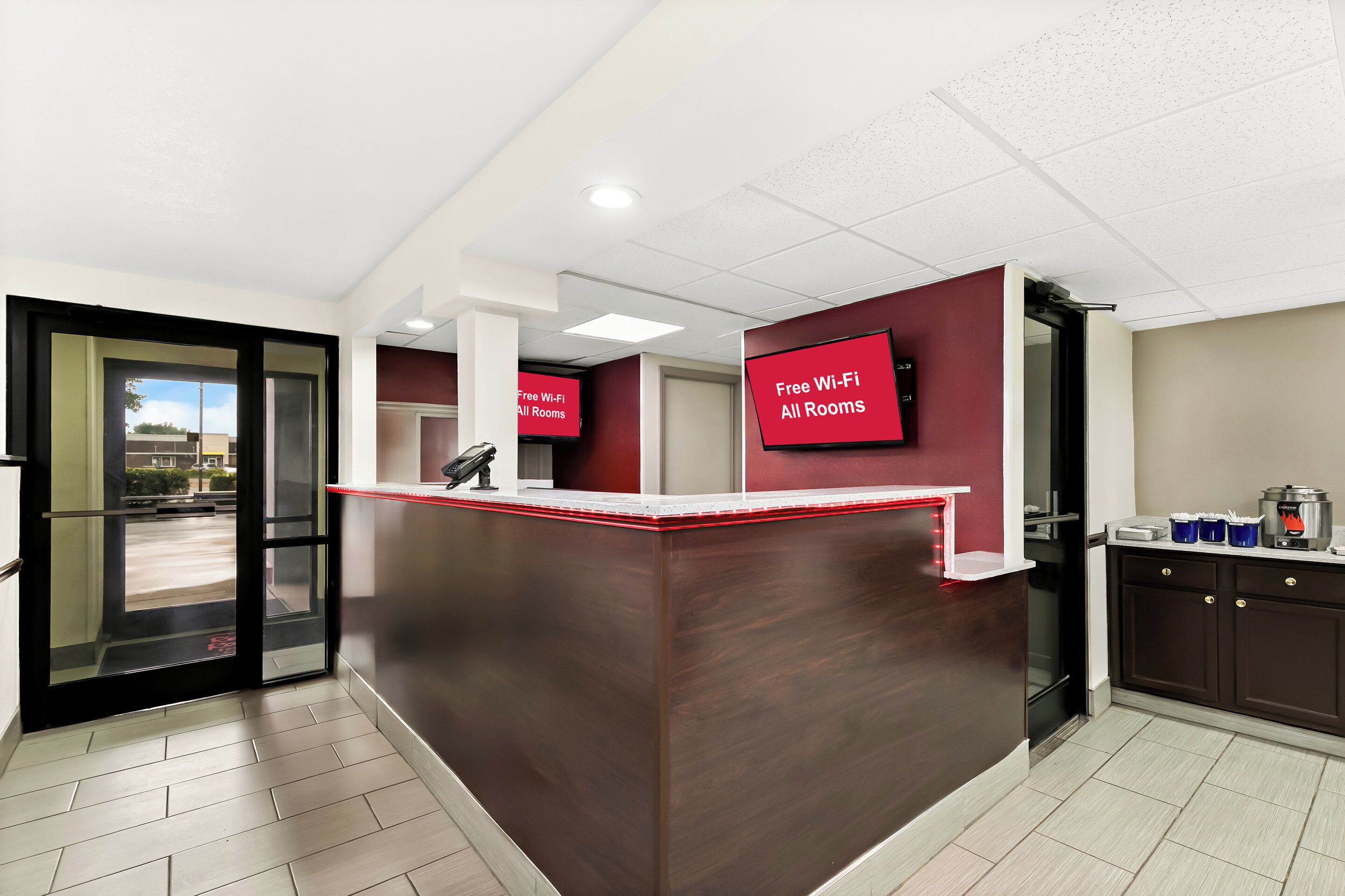A reception area with a dark wooden counter, a glass door entrance, and a sign indicating free Wi-Fi in all rooms.