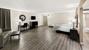 A hotel room with a bed, a desk, a chair, a sofa, a small table, a mirror, and a TV. - Red Roof Inn & Suites Duncan (Duncan)