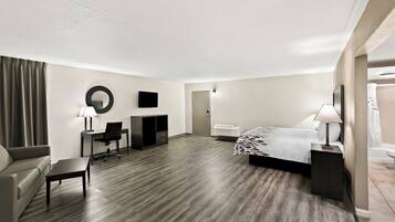 A hotel room with a bed, a desk, a chair, a sofa, a small table, a mirror, and a TV.
