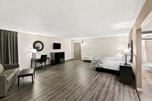 A hotel room with a bed, a desk, a chair, a sofa, a small table, a mirror, and a TV. - Red Roof Inn & Suites Duncan (Duncan)