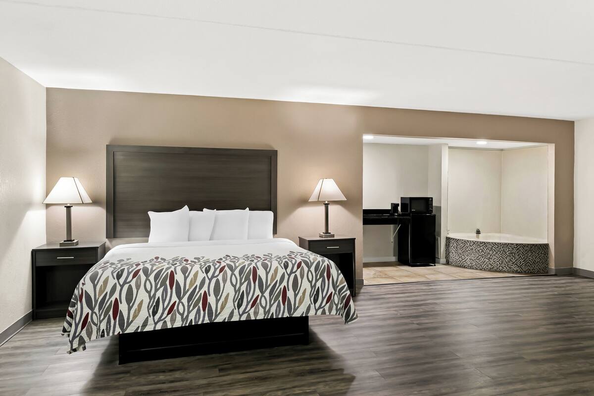 Ein Hotelzimmer mit einem Bett, zwei Nachttischen mit Lampen, einem kleinen Schreibtisch mit einem Computer und einem Badezimmer mit einer Badewanne.