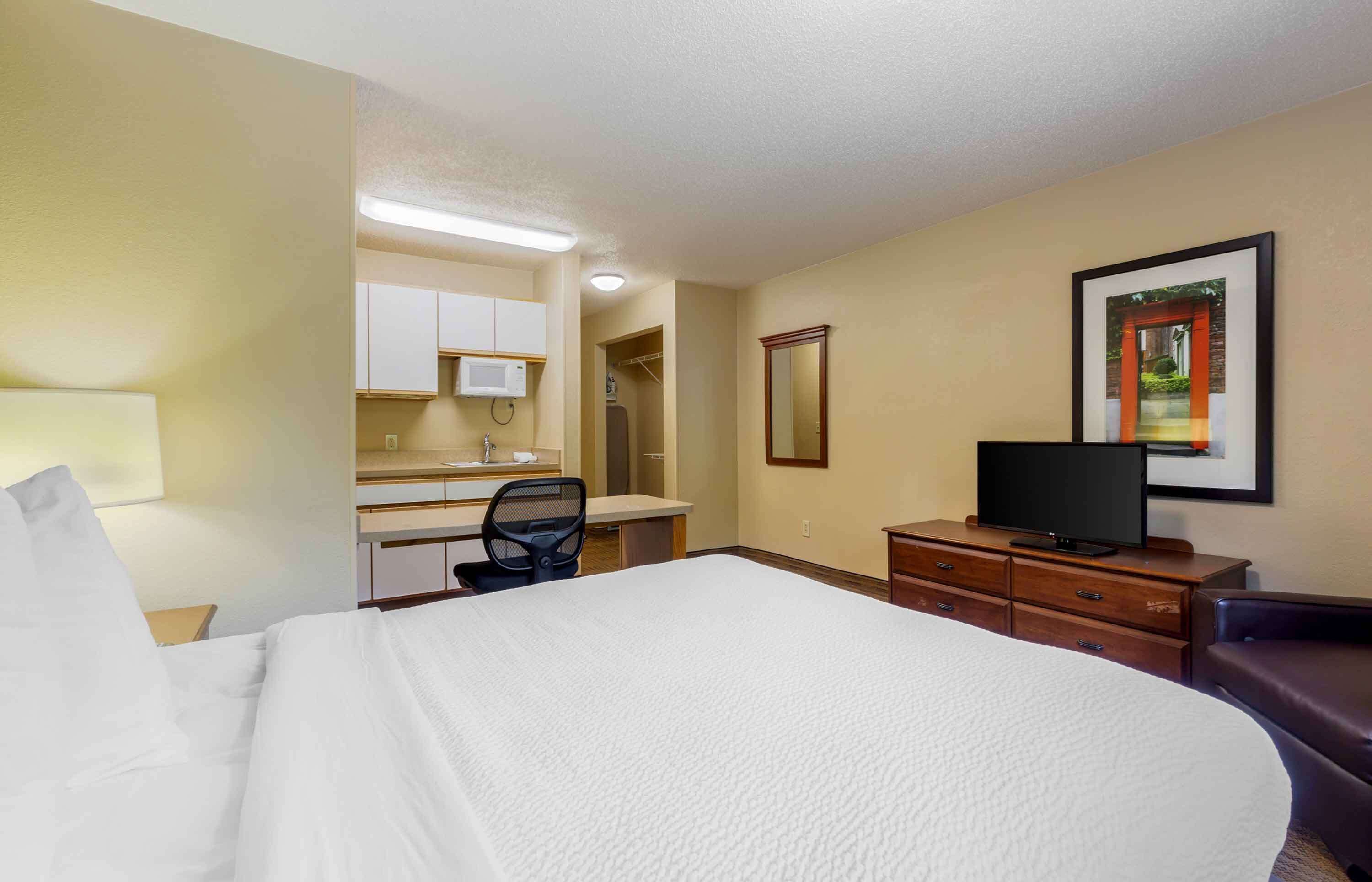 A hotel room with a bed, a desk with a chair, a television, a dresser, and a framed picture on the wall.