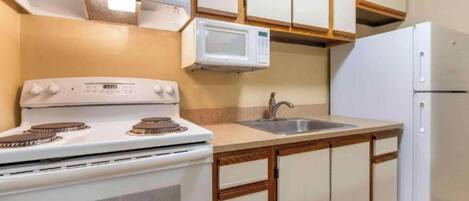 A compact kitchen with a stove, microwave, sink, and refrigerator.