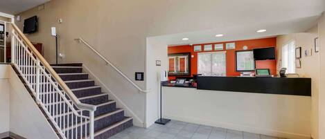 A hotel lobby with a reception desk, a staircase, and a flat-screen TV mounted on the wall.