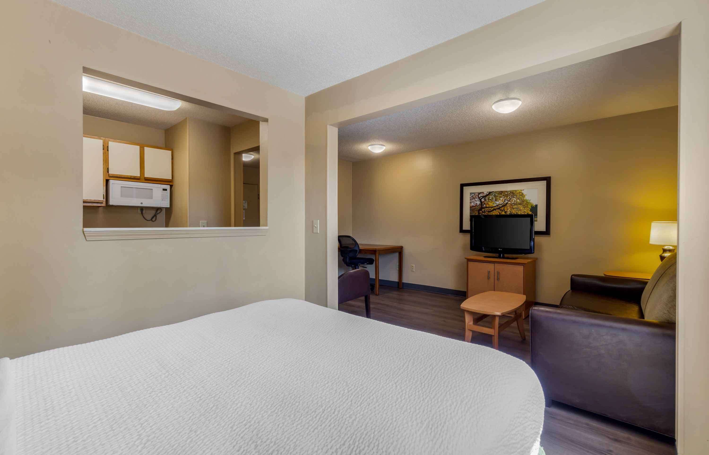 A hotel room with a bed, a desk, a chair, a sofa, a television, and a framed picture on the wall.
