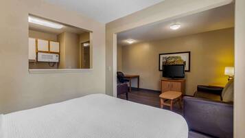 A hotel room with a bed, a desk, a chair, a sofa, a television, and a framed picture on the wall.
