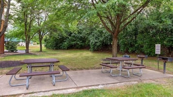 A park with picnic tables and benches, surrounded by trees and greenery.