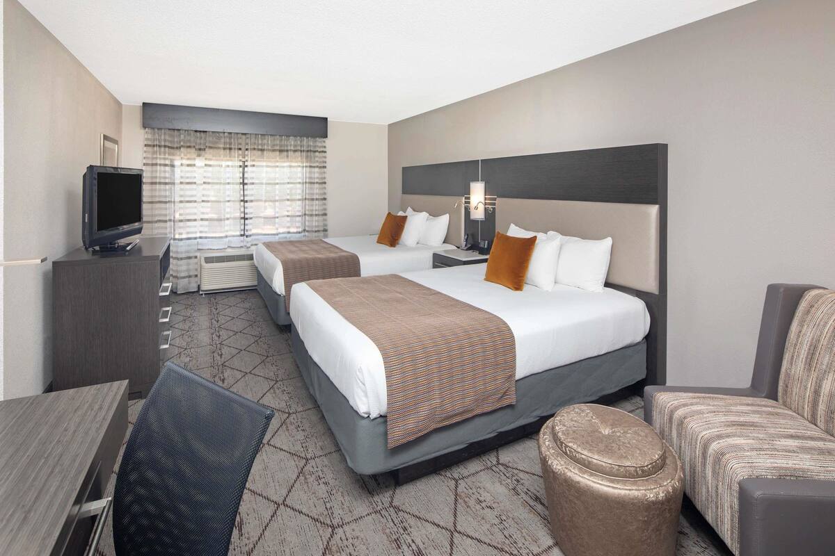 A hotel room with two beds, a TV, a desk, and a chair.