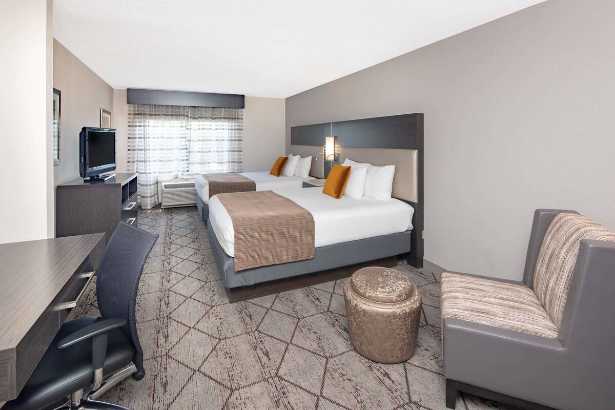 A hotel room with a bed, two bedside tables, a TV, a desk, a chair, and a sofa.