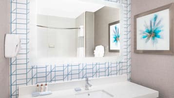 Een badkamer met een grote spiegel, een wastafel met toiletartikelen en een blauwe backsplash van geometrische tegels.