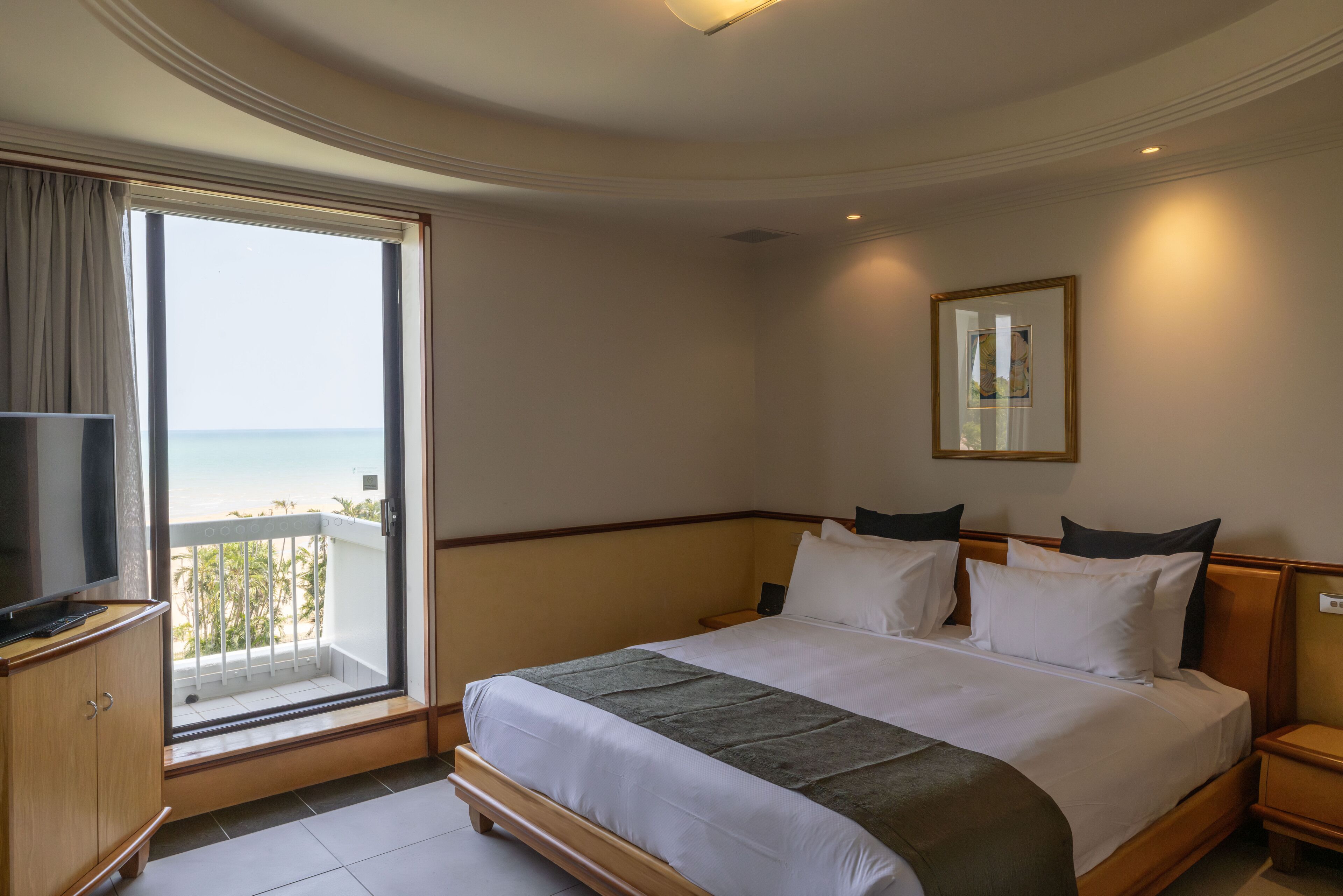 A hotel room with a large bed, a TV, a balcony with a view of the sea, and a mirror on the wall.