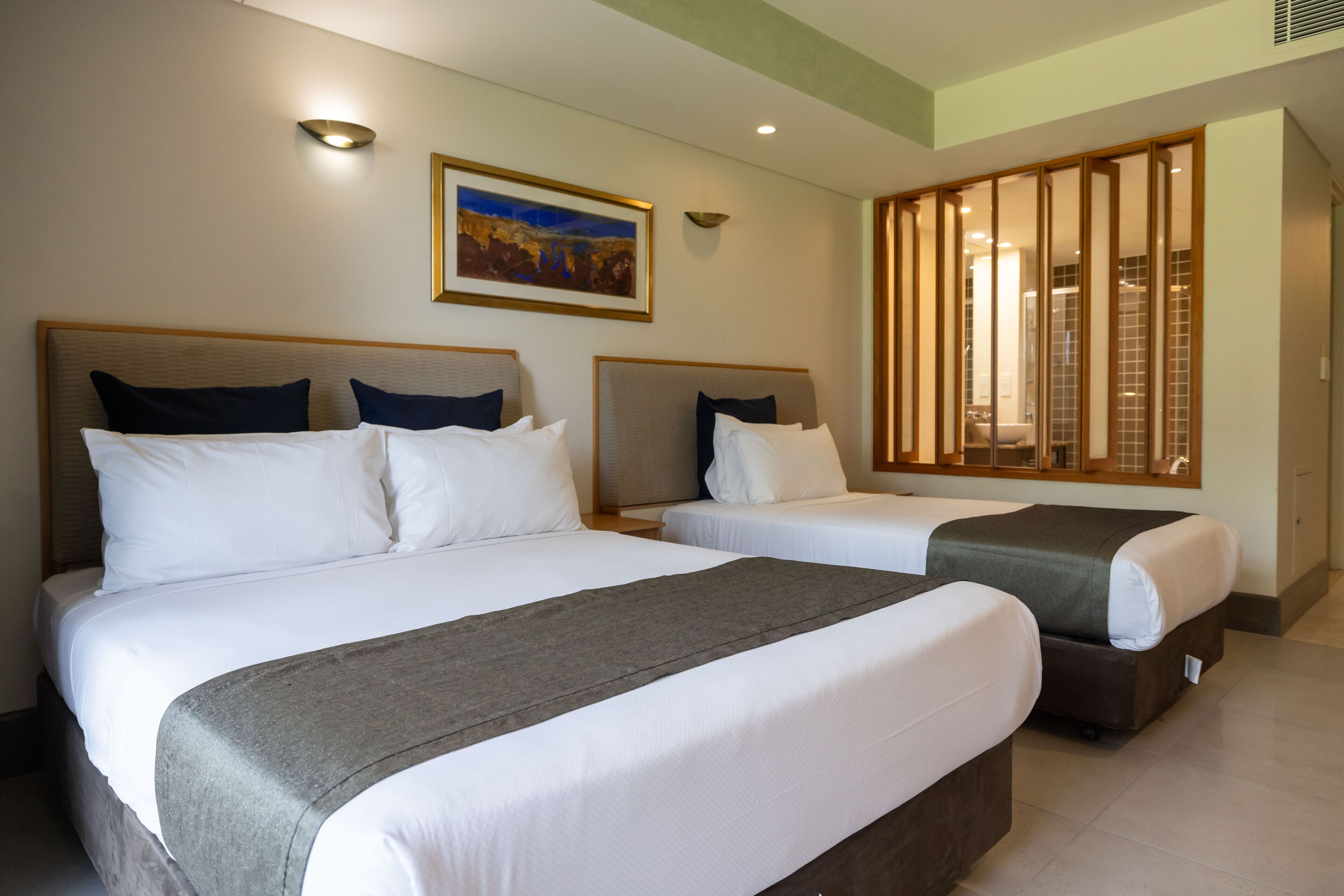 Een hotelkamer met twee bedden, een schilderij aan de muur en een schuifdeur naar een badkamer.