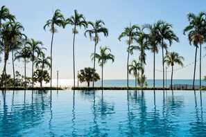 Vista a la piscina con palmeras y cielo despejado.