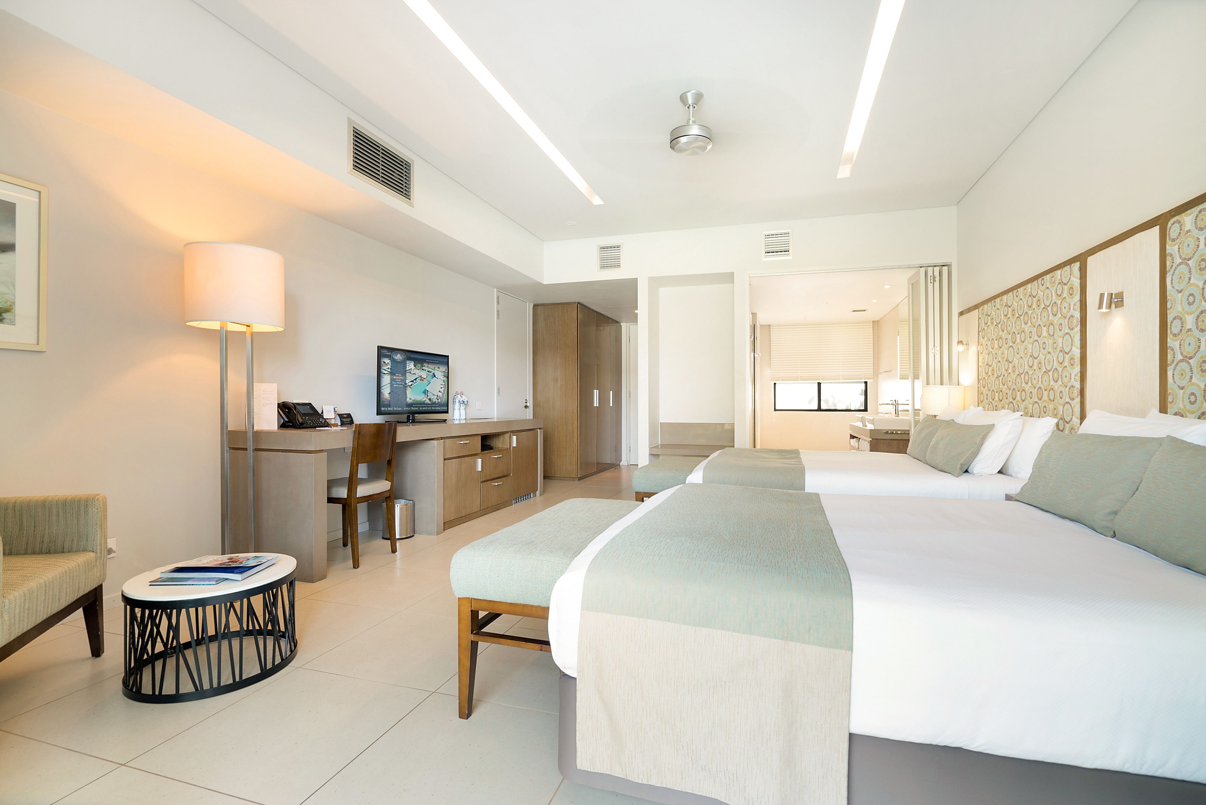 A modern hotel room with a large bed, a desk with a computer, a chair, and a small table with a lamp.