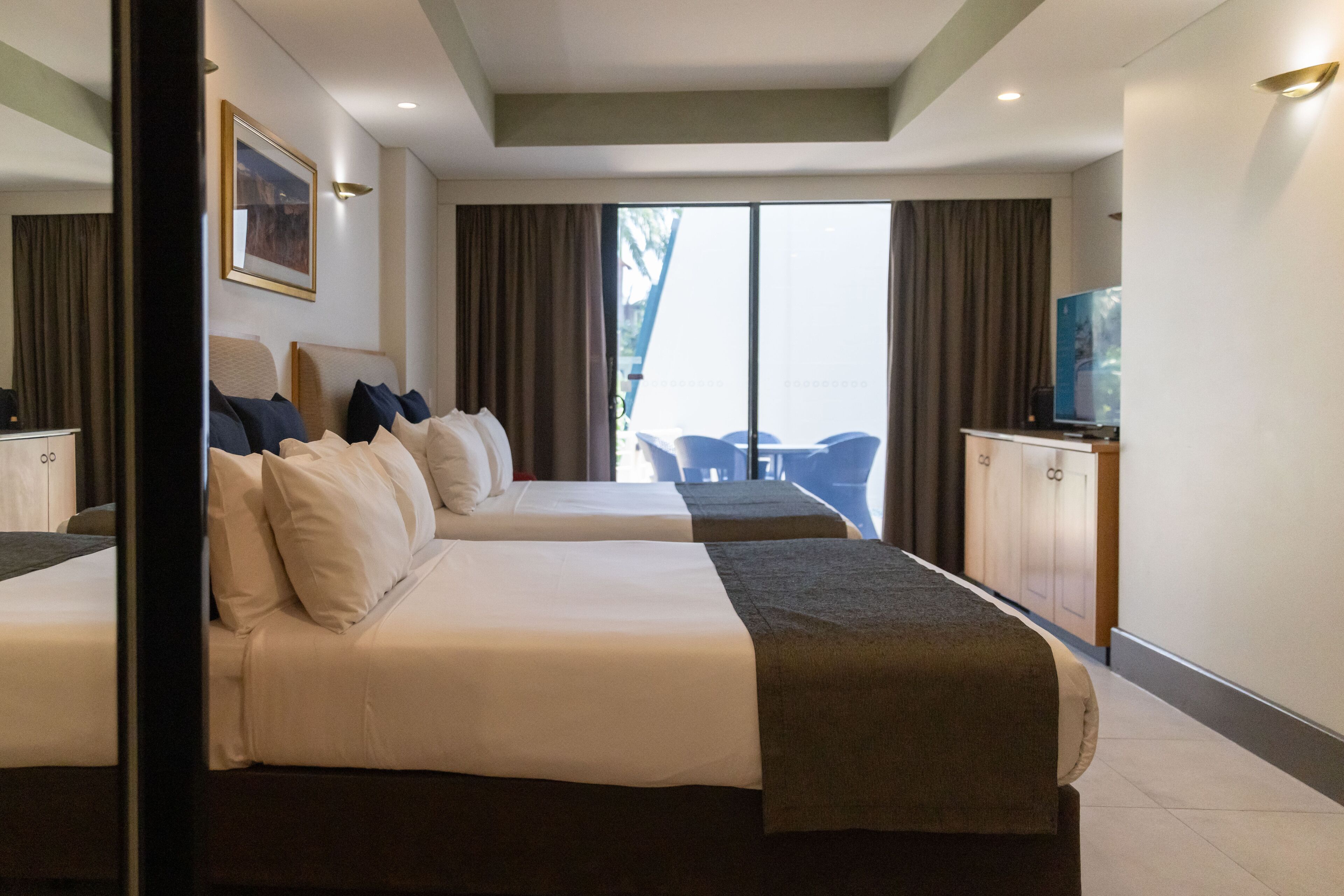 A hotel room with two beds, a TV, and a view of the outdoors.