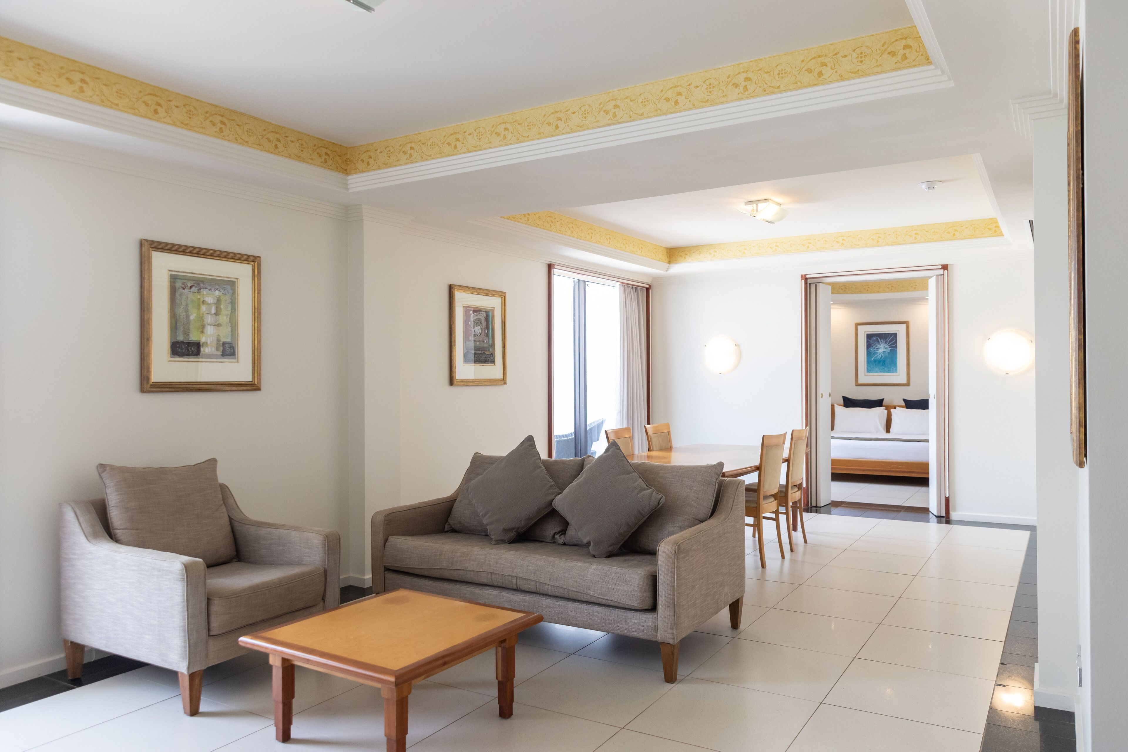 Un salón espacioso con sofá, sillón y mesa de centro. En el fondo, hay un comedor con sillas y una mesa.