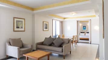 Un salón espacioso con sofá, sillón y mesa de centro. En el fondo, hay un comedor con sillas y una mesa.