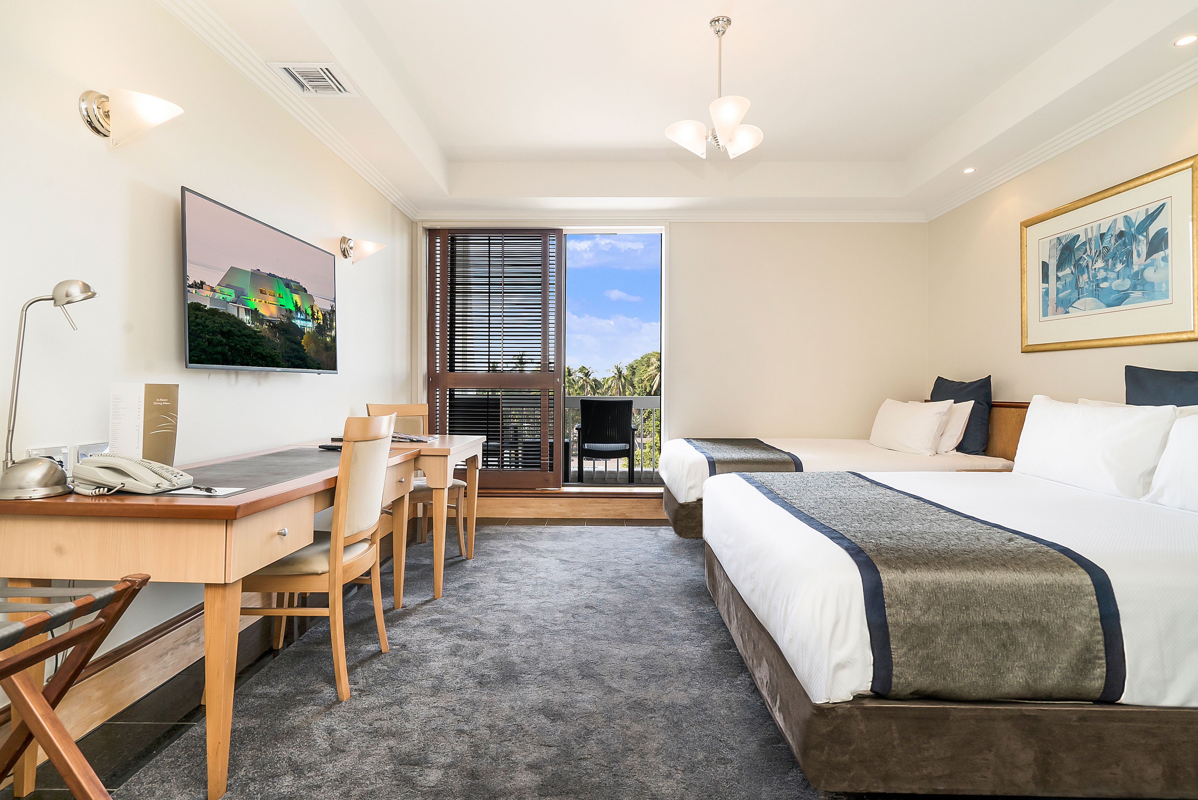 Quarto de hotel com escrivaninha, cadeira, cama e vista para o exterior.