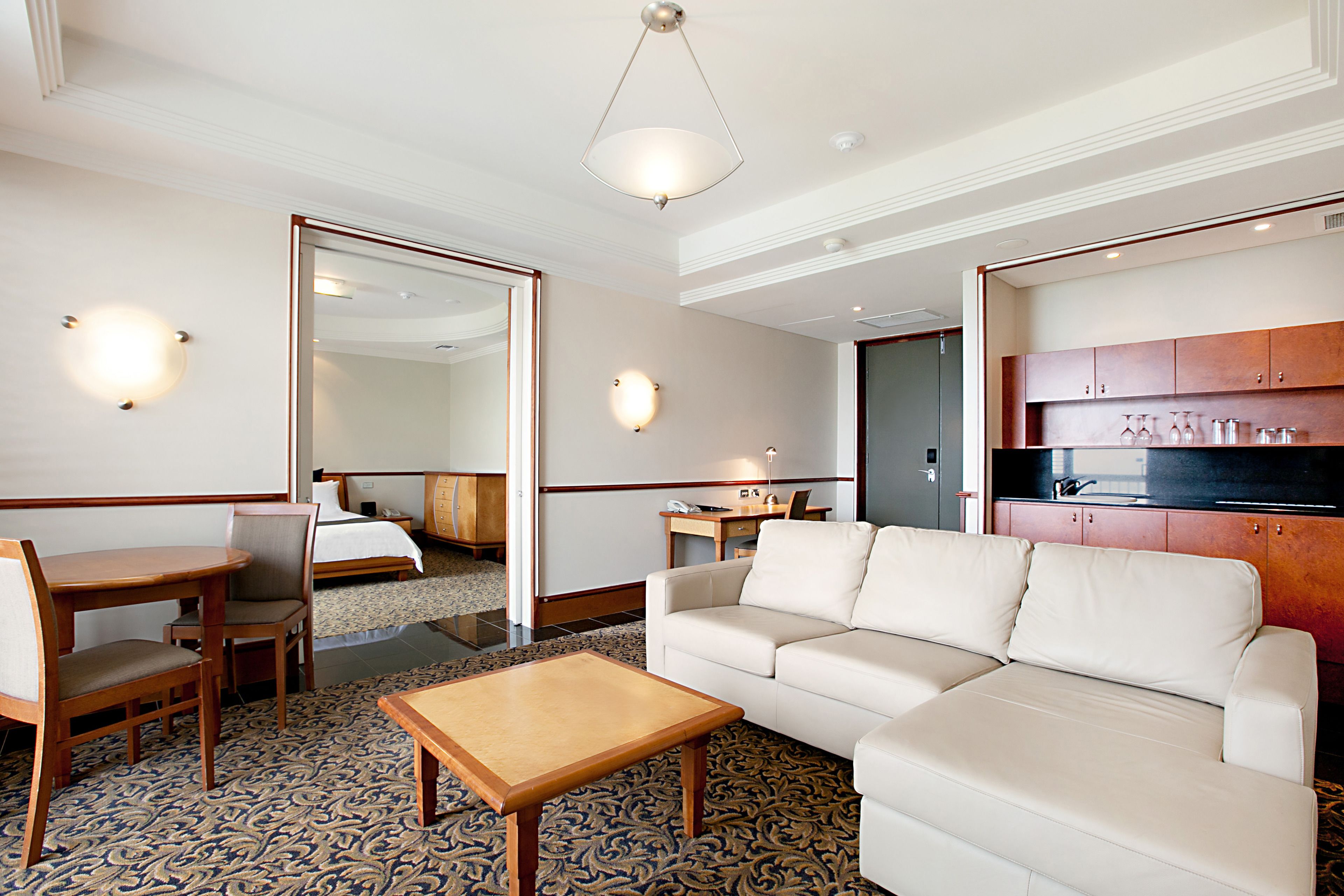 Een hotelkamer met een bank, een houten tafel, een bureau met stoel, een minibar en een grote spiegel.