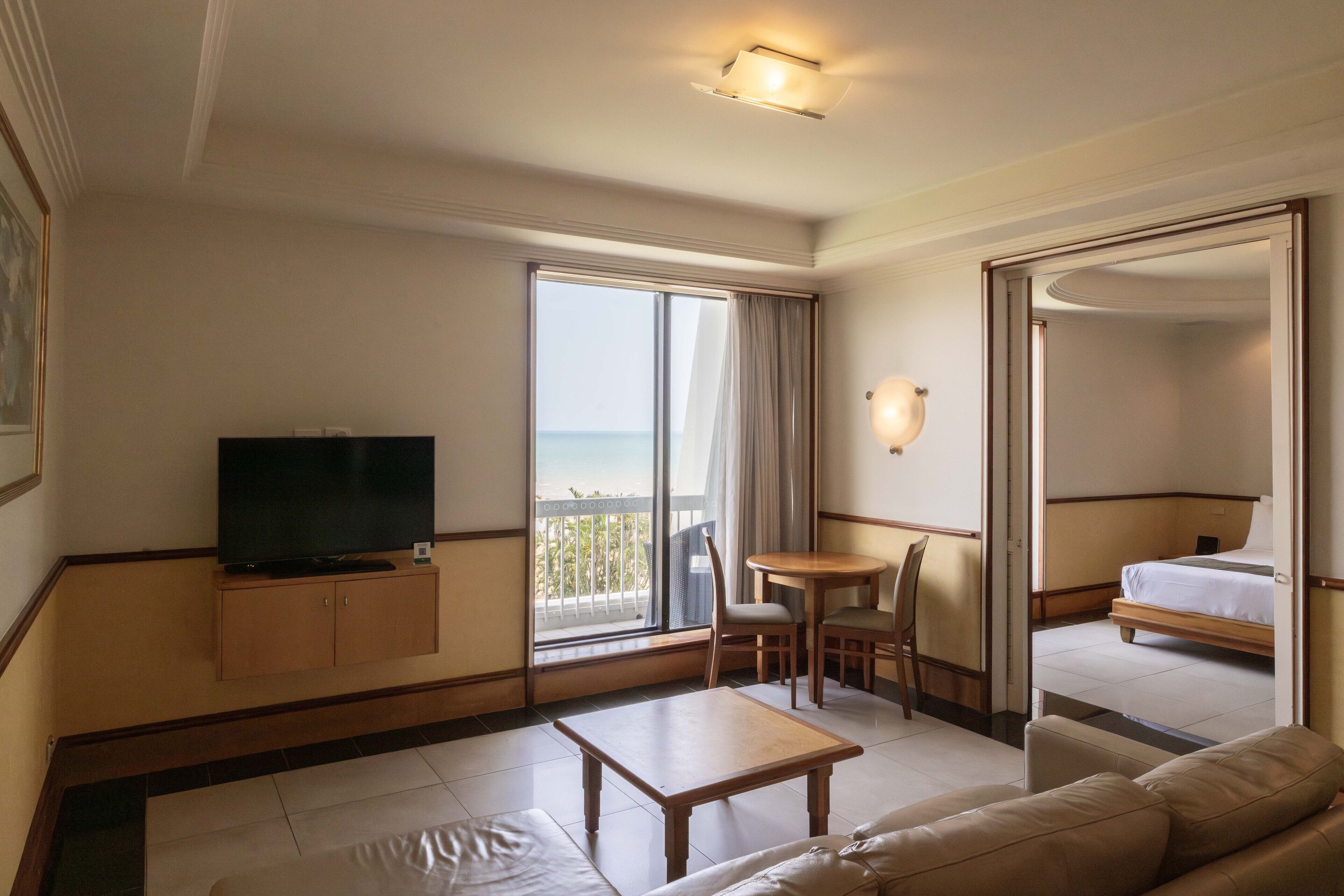 Quarto de hotel com televisão, sofá, mesinha, varanda e vista para o mar, além de uma cama.