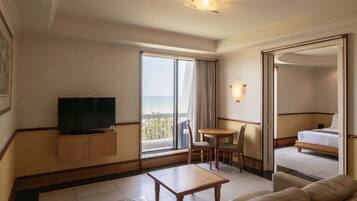 Quarto de hotel com televisão, sofá, mesinha, varanda e vista para o mar, além de uma cama.