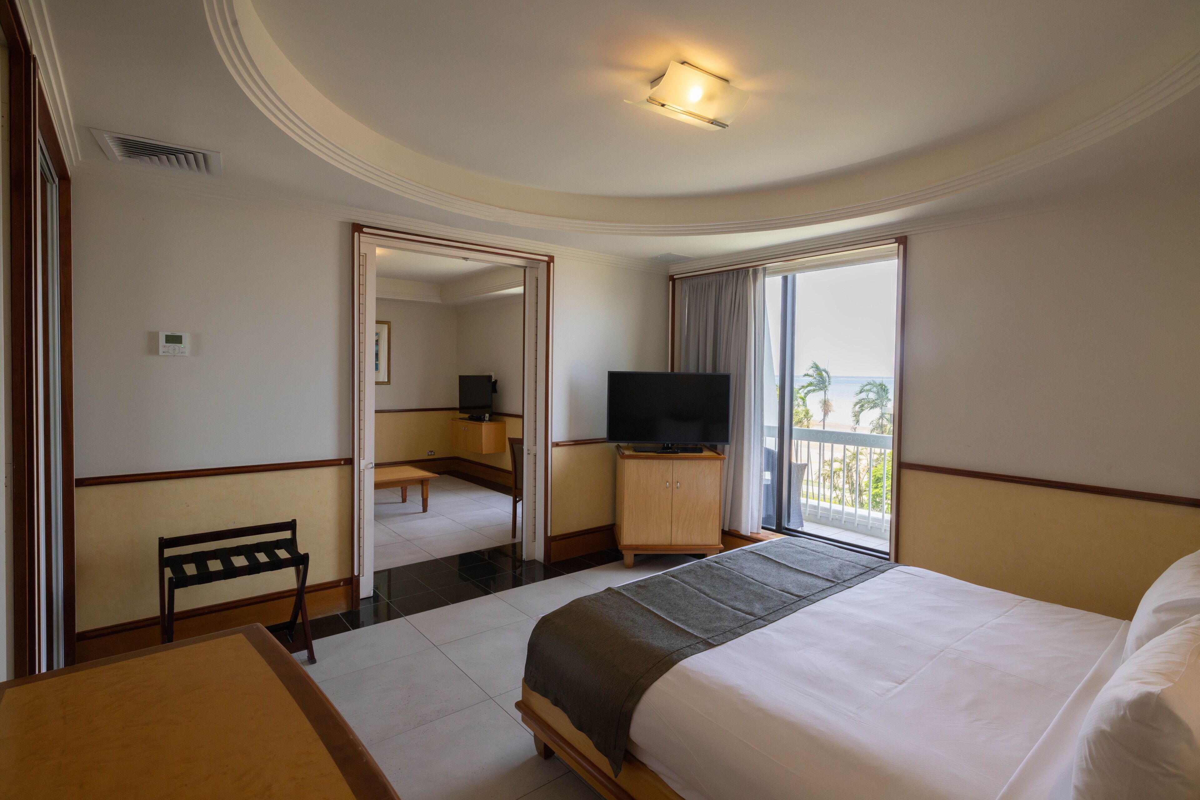 A hotel room with a bed, a desk, a chair, a television, and a balcony with a view.