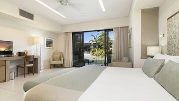 A modern hotel room with a large bed, a desk, a chair, and a balcony with a view of palm trees.