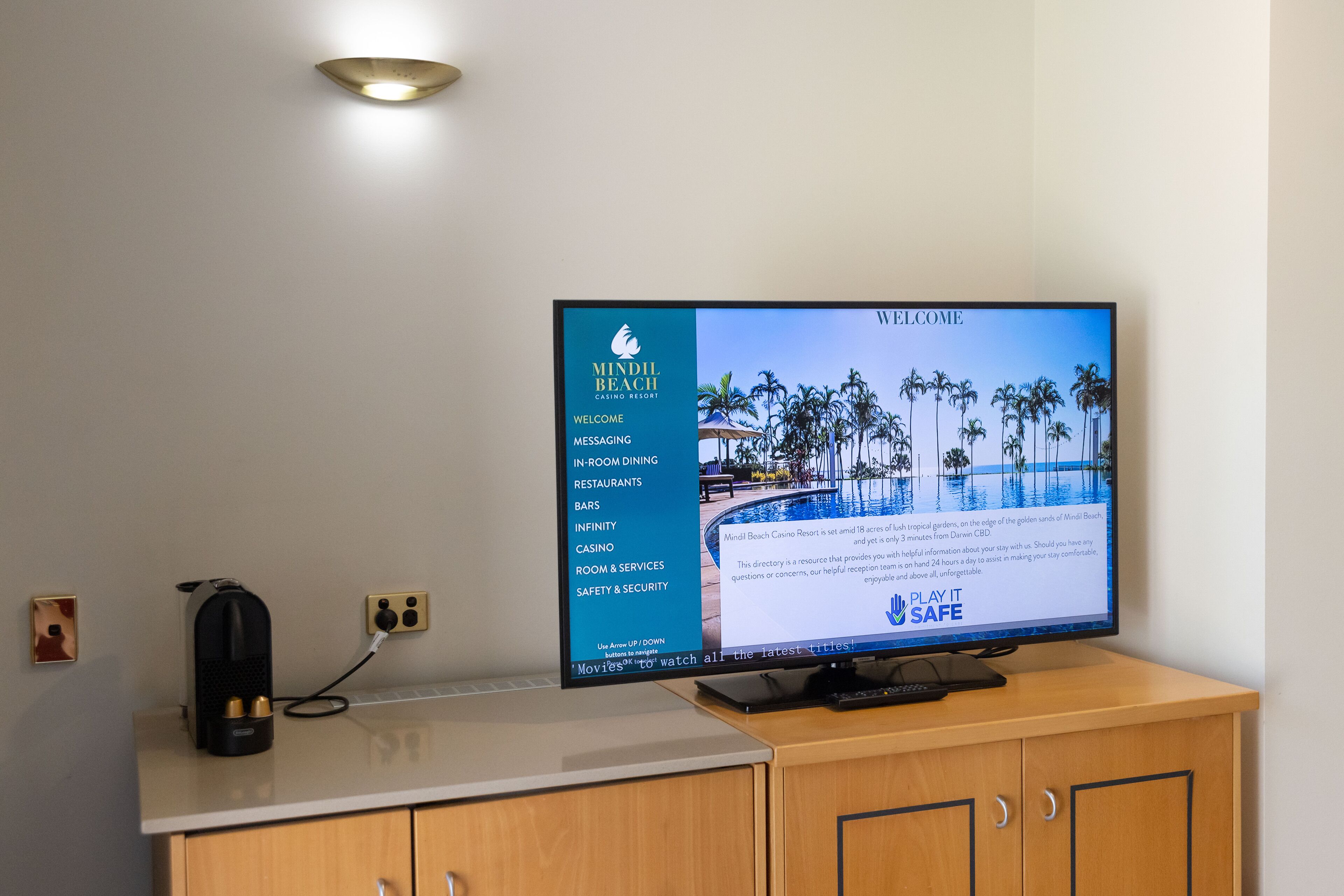 A flat-screen TV on a wooden cabinet displaying a welcome message for Mindil Beach Casino Resort, featuring amenities like in-room dining, bars, and a casino.