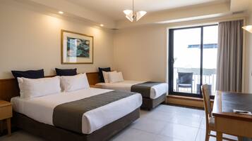 A hotel room with two beds, a dining table, and a large window with a view.