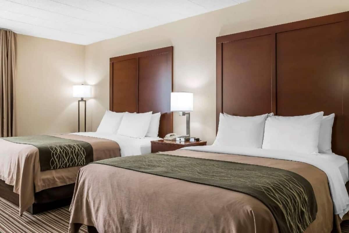 Una habitación de hotel con dos camas, cada una con cabecero de madera, lámparas de noche y un teléfono en la mesita de noche.