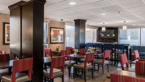 Un comedor de hotel con varias mesas y sillas, un pilar grande y una pantalla de televisión.