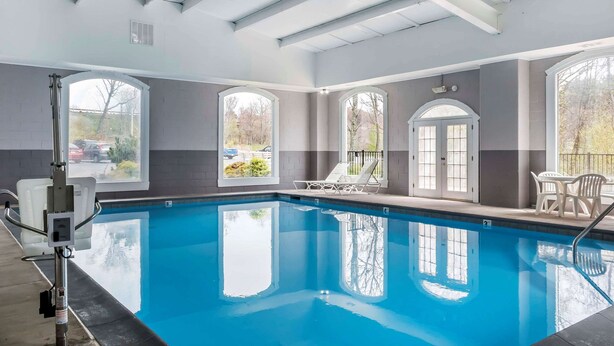 Una piscina interior con ventanas amplias, una silla de salvavidas y una zona junto a la piscina con sillas.