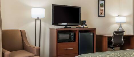 A hotel room with a bed, a desk with a computer, a television, a microwave, a refrigerator, and two lamps.