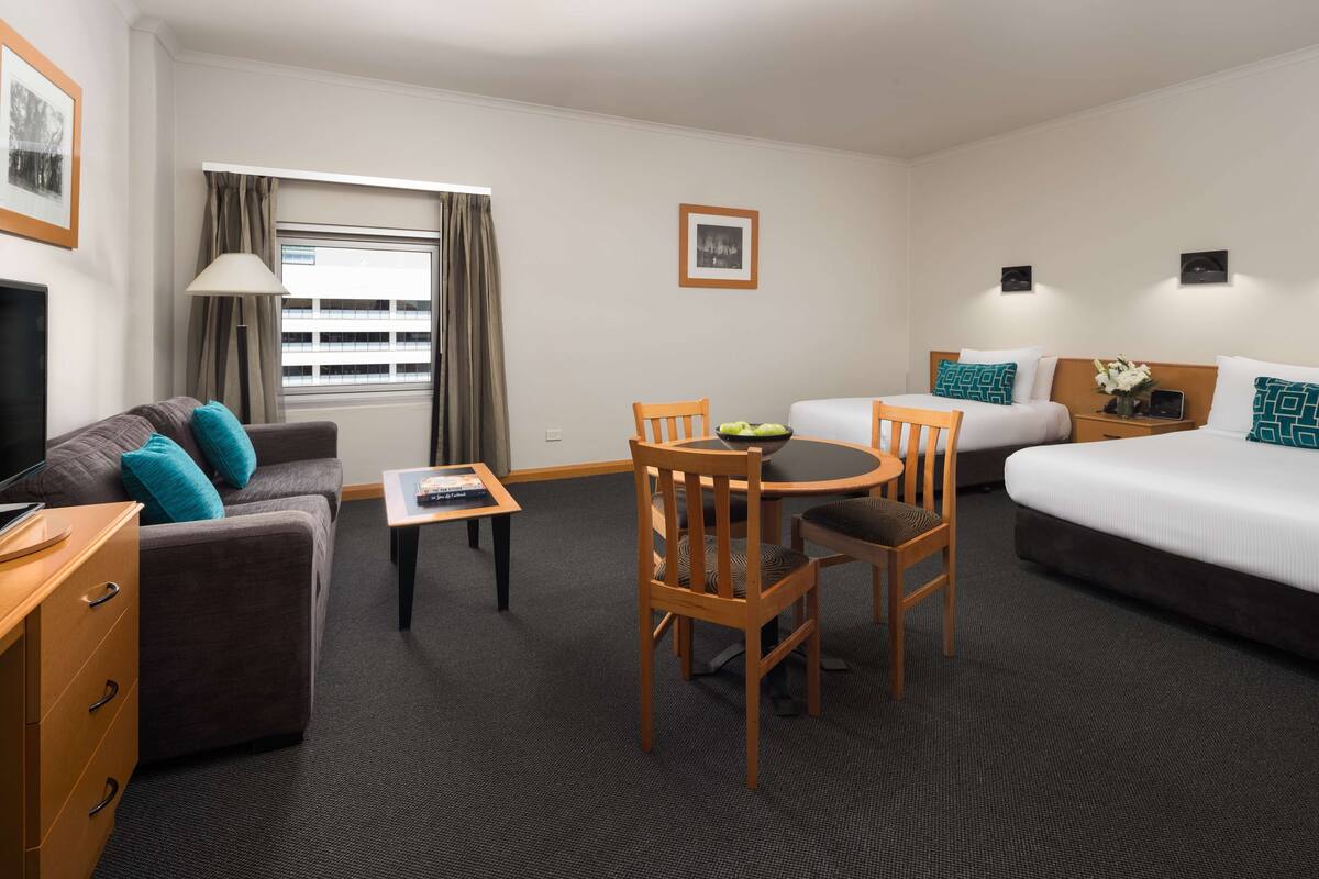 Habitación de hotel con sofá, cama, mesa de comedor con sillas, televisor y ventana con cortinas.