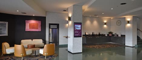 A modern lobby with a reception desk, seating area, and a staircase.