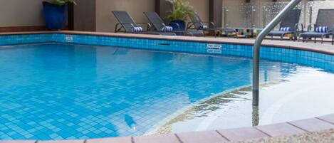 Una piscina con bordi piastrellati, sedie a sdraio e piante in vaso.