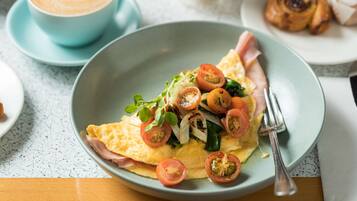 A plate of food with a slice of ham, tomatoes, and greens, a cup of coffee, and a pastry on a table.