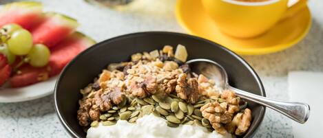 Un tazón de yogur con nueces y semillas, un plato de sandía y uvas, y una taza de café sobre una mesa.
