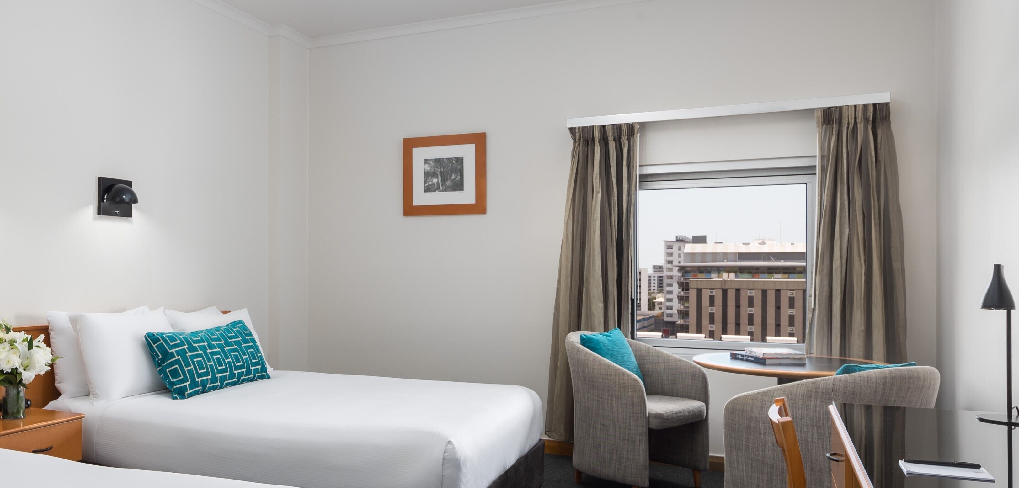 Een hotelkamer met een bed, een stoel, een bureau, een lamp en een raam met gordijnen.