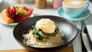 Une table dressée pour le petit-déjeuner avec un sandwich, une tasse de café et une assiette de fruits.