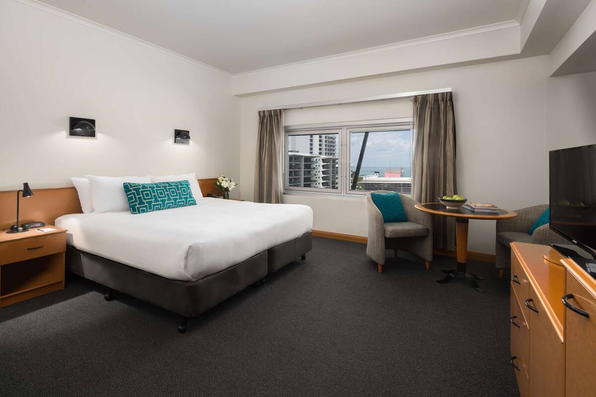 Habitación de hotel con cama, escritorio, silla, televisor y ventana con cortinas.