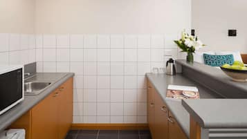 A compact kitchen with a microwave, coffee maker, and a bowl of fruit on the counter.