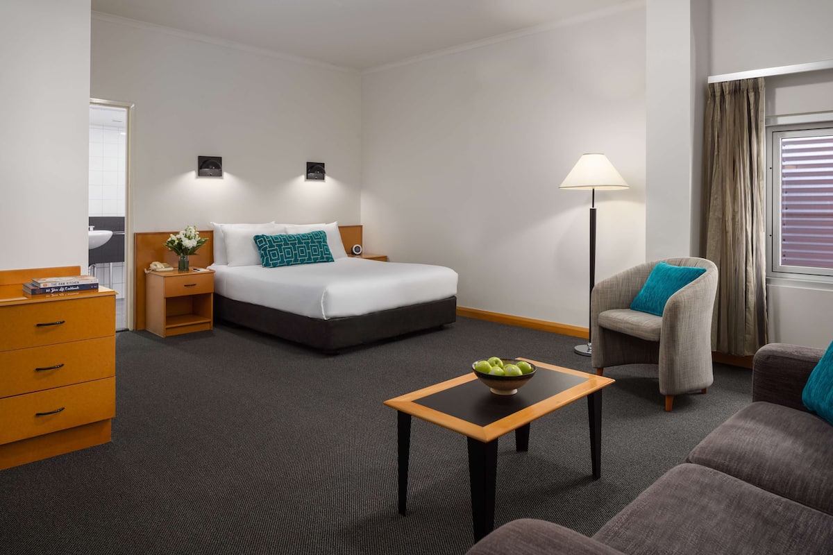 Una habitación de hotel con cama, escritorio, silla, sofá y lámpara.