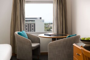 A hotel room with two armchairs, a small round table with a book, and a bowl of fruit on a dresser.
