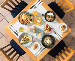 Una mesa de comedor con diversos alimentos para el desayuno, incluyendo huevos, tostadas, fruta y bebidas.