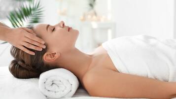 A person lying on a white bed with a rolled white towel beside them.